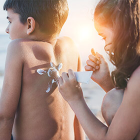 a sister applying suncream to her siblings back on the beach