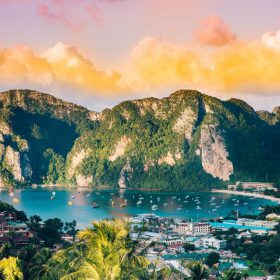 Large cliffs with water and boats below in front of sunset sky